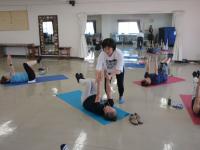 仰向きで膝を直角に曲げ両手を天井に向けて伸ばしているのを講師が矯正している