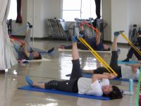 仰向けに寝て片足を天井に向け伸ばし、足裏に紐をかけて引っ張っている